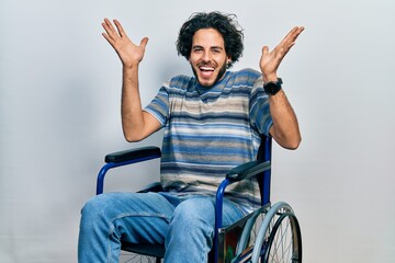 Sticker - Handsome hispanic man sitting on wheelchair celebrating crazy and amazed for success with arms raised and open eyes screaming excited. winner concept