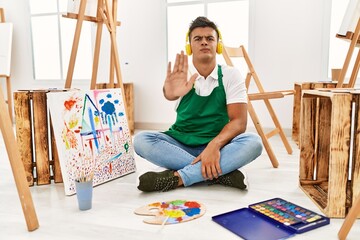 Sticker - Young hispanic man at art studio doing stop sing with palm of the hand. warning expression with negative and serious gesture on the face.