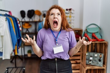 Sticker - Young redhead woman working as manager at retail boutique crazy and mad shouting and yelling with aggressive expression and arms raised. frustration concept.