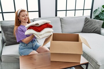 Sticker - Young redhead woman smiling confident holding folded clothes at home