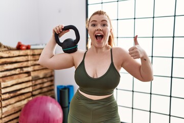 Poster - Young redhead woman wearing sportswear using dumbbells smiling happy and positive, thumb up doing excellent and approval sign