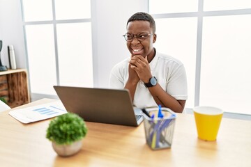 Poster - Young african man working at the office using computer laptop laughing nervous and excited with hands on chin looking to the side