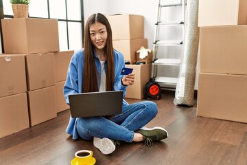 Canvas Print - Young chinese girl using laptop and credit card sitting on the floor at new home