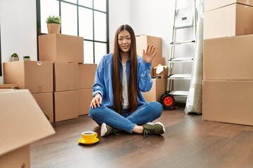 Poster - Young chinese girl saying hello with hand sitting on the floor at new home