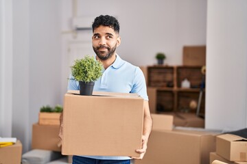 Poster - Hispanic man with beard moving to a new home holding box smiling looking to the side and staring away thinking.