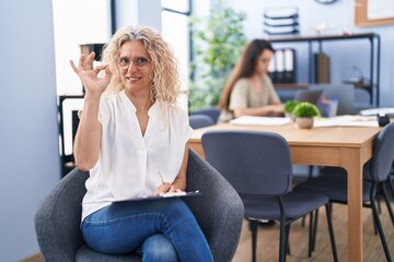 Poster - Middle age woman working at the office holding clipboard doing ok sign with fingers, smiling friendly gesturing excellent symbol