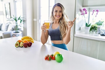 Poster - Young caucasian fitness woman wearing sportswear drinking healthy orange juice smiling happy pointing with hand and finger to the side