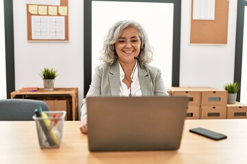 Wall Mural - Middle age businesswoman sitting on desk working using laptop at office with a happy and cool smile on face. lucky person.