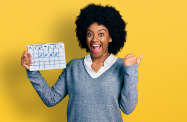 Sticker - Young african american woman holding travel calendar pointing thumb up to the side smiling happy with open mouth