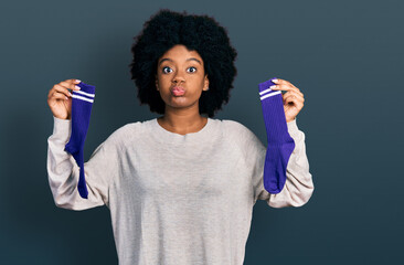 Sticker - Young african american woman holding socks puffing cheeks with funny face. mouth inflated with air, catching air.