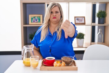 Canvas Print - Caucasian plus size woman eating breakfast at home looking unhappy and angry showing rejection and negative with thumbs down gesture. bad expression.