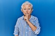 © Krakenimages.com - Senior woman with grey hair standing over blue background asking to be quiet with finger on lips. silence and secret concept.