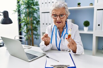 Wall Mural - Senior grey-haired woman wearing doctor uniform speaking about treatment at clinic