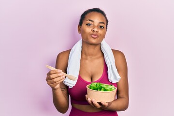 Young african american girl wearing sportswear eating salad looking at the camera blowing a kiss being lovely and sexy. love expression.