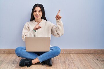 Poster - Young woman using laptop sitting on the floor at home smiling and looking at the camera pointing with two hands and fingers to the side.