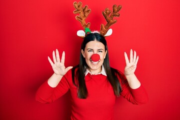 Sticker - Young hispanic woman wearing deer christmas hat and red nose showing and pointing up with fingers number nine while smiling confident and happy.