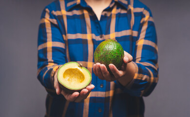 Wall Mural - Close-up of hands holding avocados while standing on a gray background