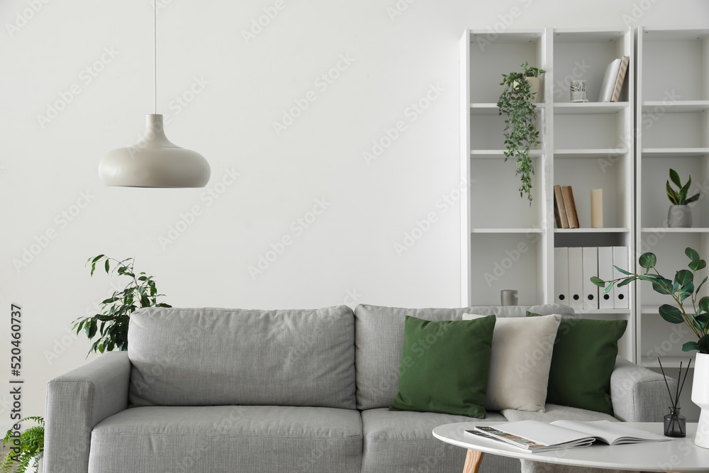 Interior of light living room with grey sofa, table and shelving unit