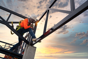 A Steel roof truss welders are working on the roof structure with safety devices to prevent fall safety at the construction site.