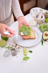 Wall Mural - Toasts preparation - woman smearing mashed avocado on a toasted bread