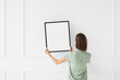 © kite_rin - Woman hold blank picture frame mockup on white wall, Artwork mock-up in minimal interior design, Minimal photographer artist concept.