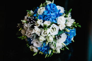 Wedding bouquet of the bride of blue and white flowers and greens lying on black background. Close up.