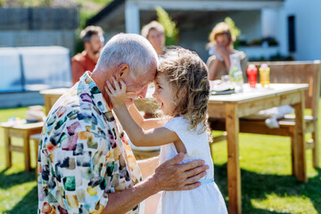 Wall Mural - Happy little girl embracing her grandfather at generation family birthday party in summer garden.