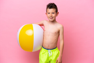 Wall Mural - Little caucasian boy holding a beach ball isolated on pink background smiling a lot