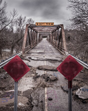 Vertical Shot Of A Broken Old Road On A Bridge With Closed Red Signs
