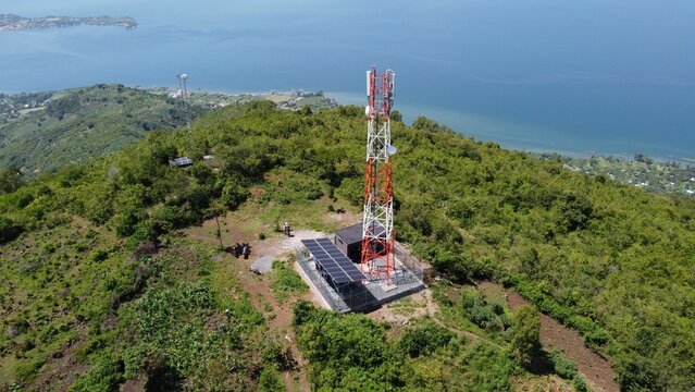 Aerial view of a telecommunication tower and solar panels on top of a forested mountain on the coast