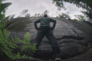 A man stands in front of an insurmountable vertical granite wall. low angle