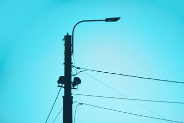 A dark silhouette of a street lamp against a clear blue sky. Street lighting and electrification. Technologies.