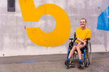 Disabled person in a public park in a wheelchair, wearing a yellow t-shirt smiling