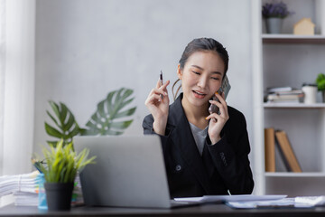 Portrait of young Asian smiling cheerful entrepreneur in casual office making a phone call while working with a laptop