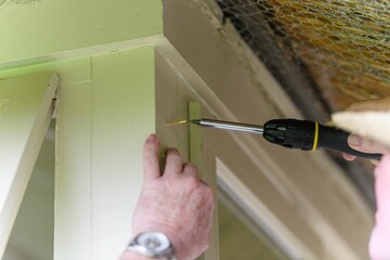 Wall Mural - Male hand screwing a nail into a wall with a screwdriver