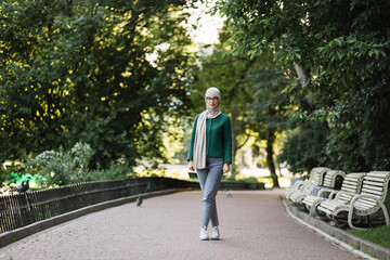 Wall Mural - Full length portrait of beautiful smiling stylish muslim woman with in hijab walking in summer city park. Street style, summer, outdoor, break concept. Walking down the sunny park.