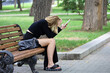Blonde girl wearing black clothes sitting on wooden bench with smartphone in hand, summer leisure in city