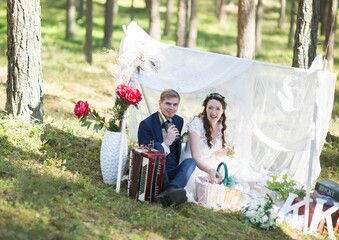 Wall Mural - View of groom and bride sitting and looking at camera in park decorated for wedding