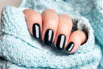 Wall Mural - Female hand in blue knitted sweater with beautiful manicure - dark black nails. Nail care concept