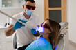 © Rabizo Anatolii - Artificial teeth whitening. Woman in red protective glasses patient do UV teeth whitening procedure. Dental ultraviolet whitening treatment with light, fluoride and laser.