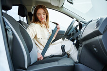 Young Woman Sits At The Wheel Of A Car And Hold Seat Belt Looks At Window. Side View