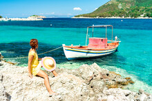 Woman Sitting On Rocks Looking At Boats In The Turquoise Sea, Porto Atheras, Kefalonia, Ionian Islands, Greek Islands, Greece