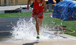 High school boy splashing as he exits the steeplechase water jump during a race