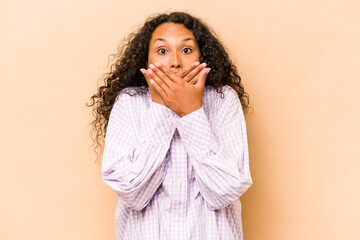 Wall Mural - Young hispanic woman isolated on beige background shocked covering mouth with hands.