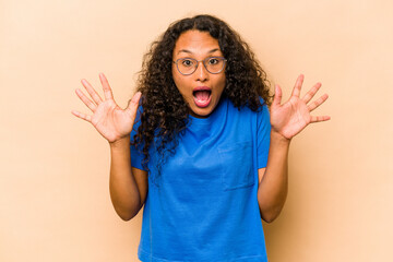 Wall Mural - Young hispanic woman isolated on beige background receiving a pleasant surprise, excited and raising hands.