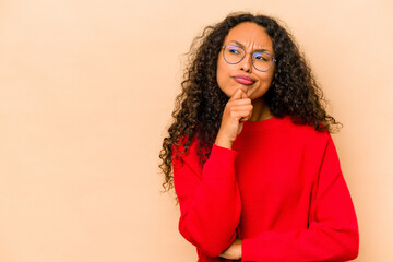 Wall Mural - Young hispanic woman isolated on beige background looking sideways with doubtful and skeptical expression.