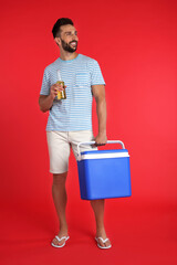 Wall Mural - Happy man with cool box and bottle of beer on red background