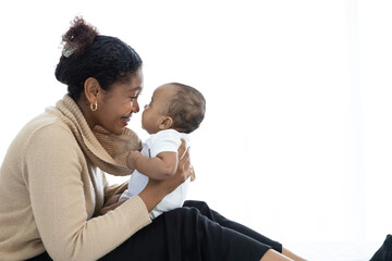 Wall Mural - African young mother carrying and kissing with her adorable baby on bed