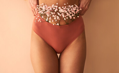 Wall Mural - Cropped image of woman in lingerie with flowers made of panties on beige background.