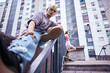 © chika_milan - Low angle view of a teenage boy sitting in urban exterior surrounded by the buildings.